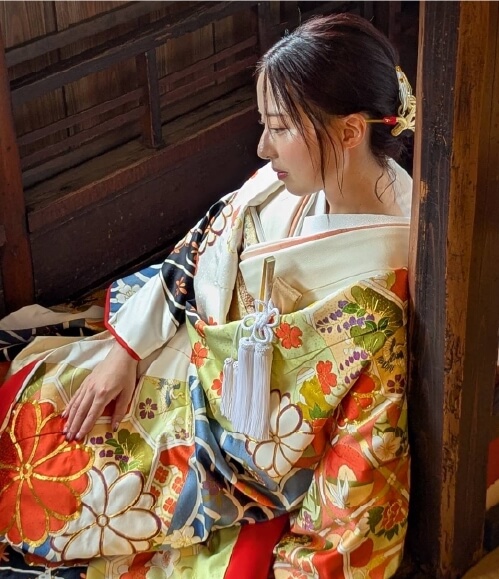 色鮮やかな花柄の振袖を着た女性が、木造の建物の中で静かに座っている様子